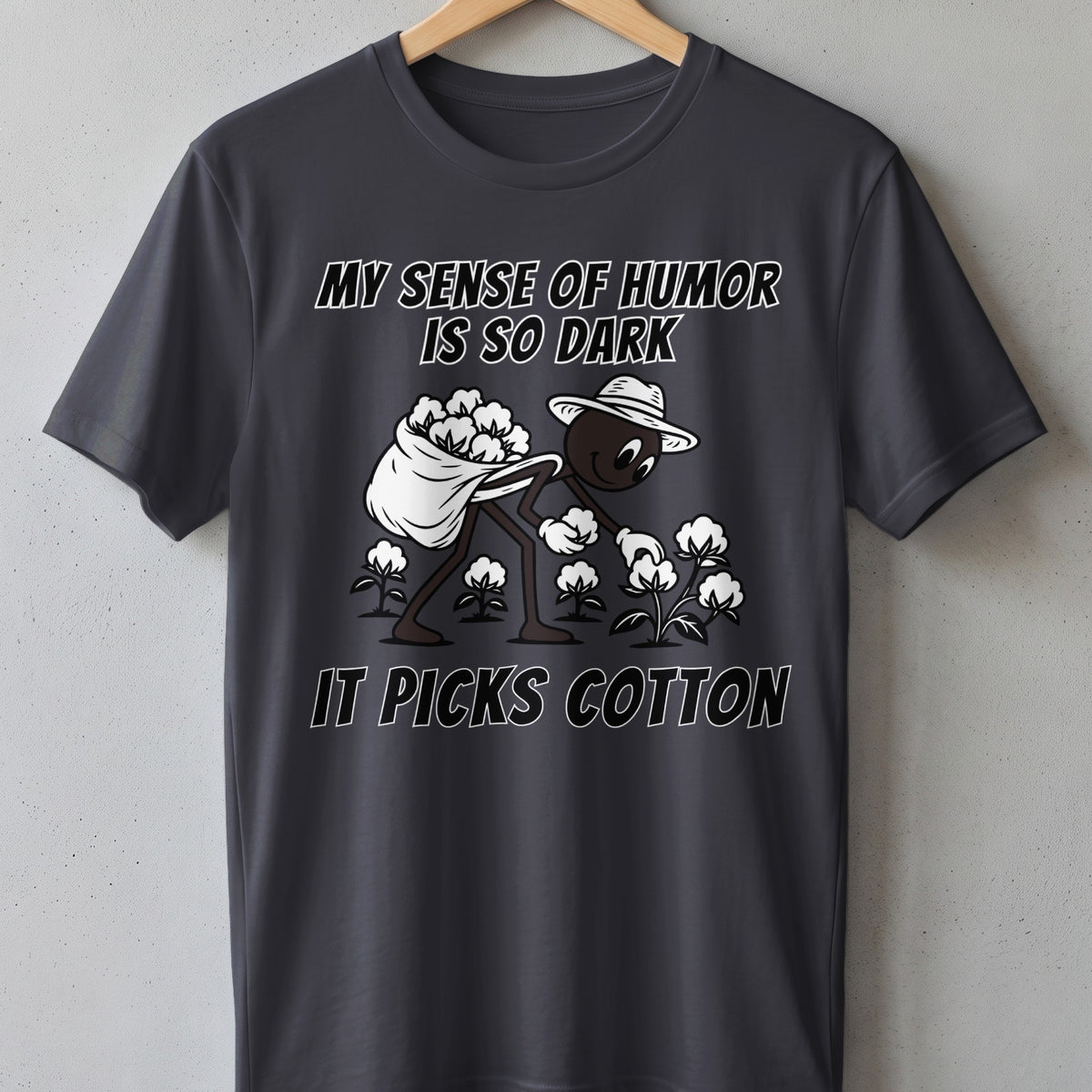 Dark gray t-shirt with cartoon character picking cotton and text "MY SENSE OF HUMOR IS SO DARK IT PICKS COTTON."