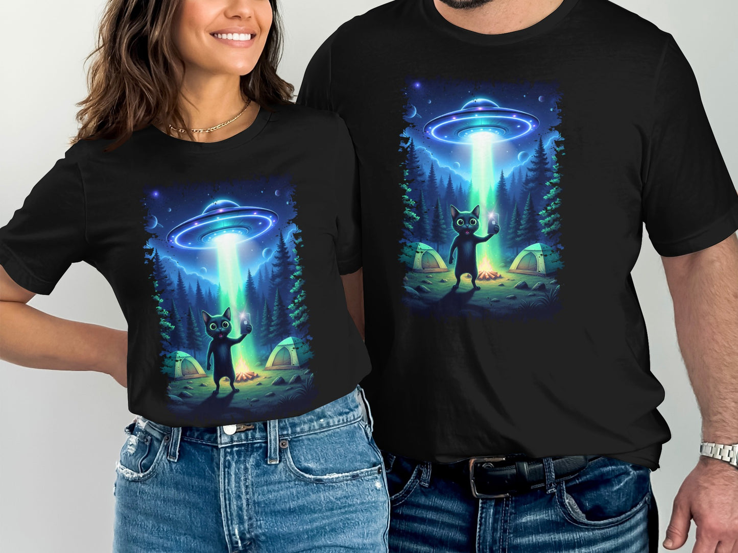 Black t-shirts show a cat taking a selfie under a UFO's beam in a forest.