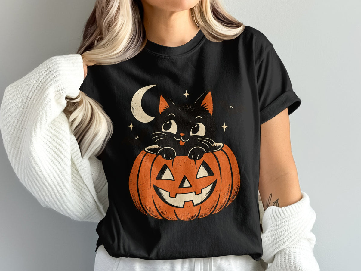 Black t-shirt with a graphic of a black cat peeking out of a jack-o'-lantern under a crescent moon.
