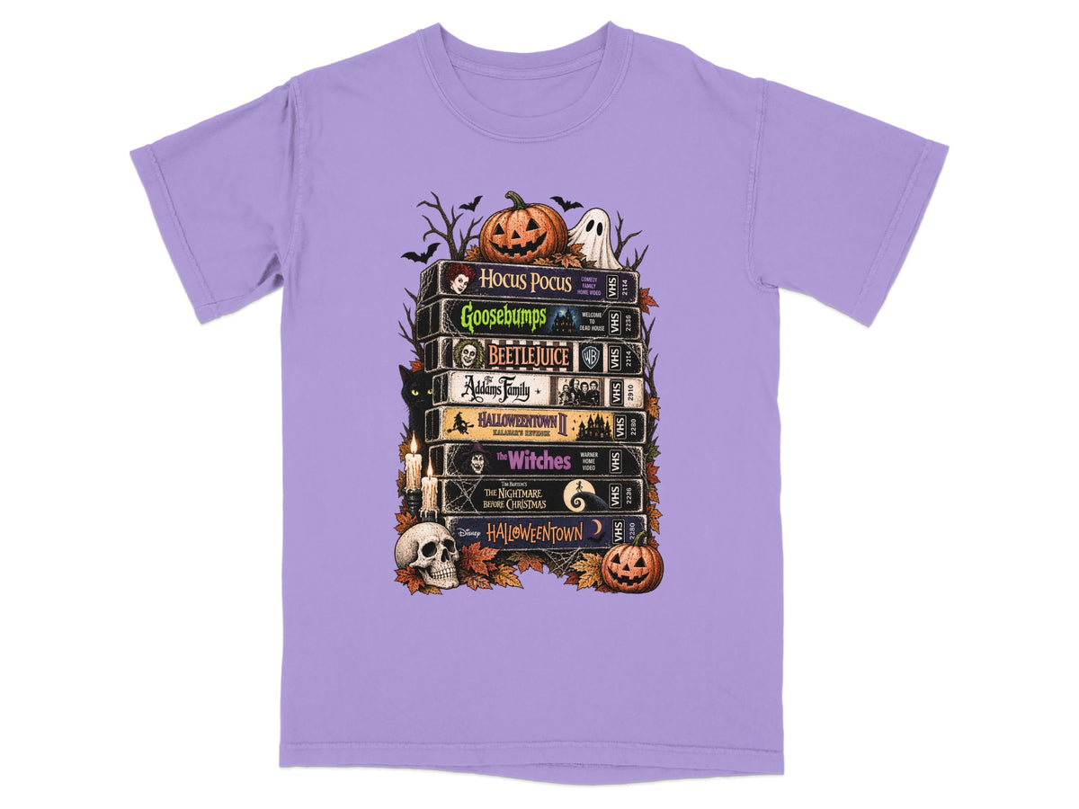 Stack of Halloween movie VHS tapes on a purple t-shirt with festive graphics.