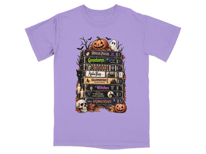 Stack of Halloween movie VHS tapes on a purple t-shirt with festive graphics.