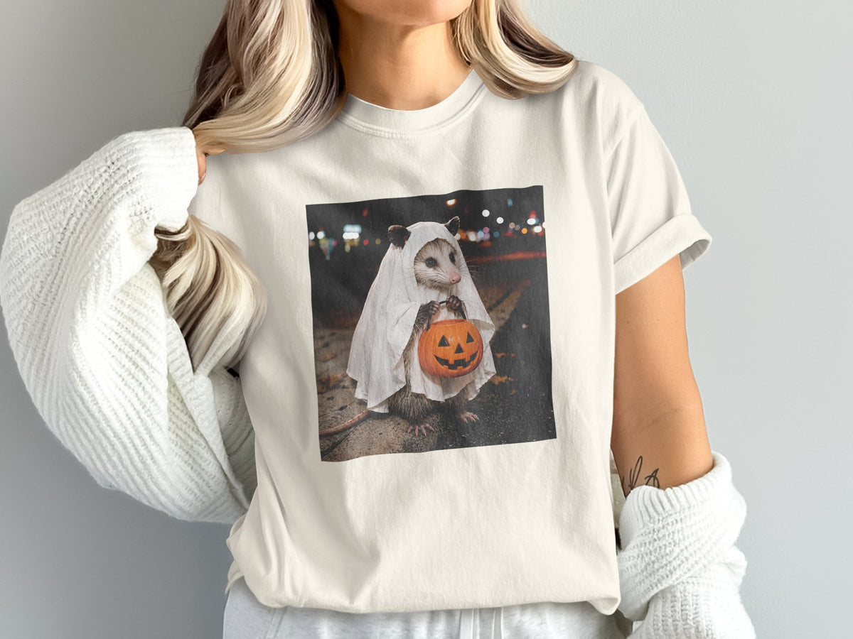 Opossum in a ghost costume holding a jack-o'-lantern candy bucket at night.
