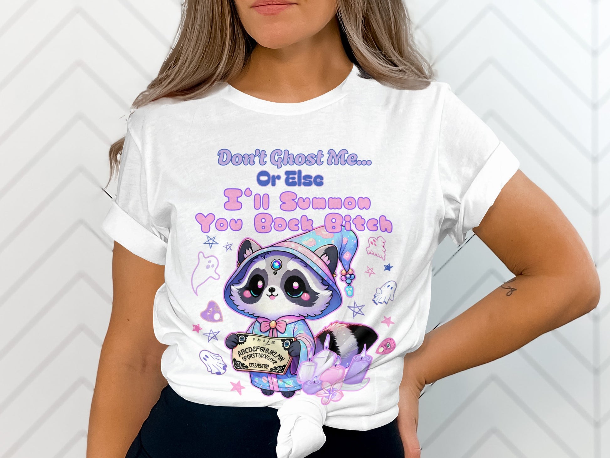 White t-shirt with a raccoon holding Ouija board, ghosts and text.