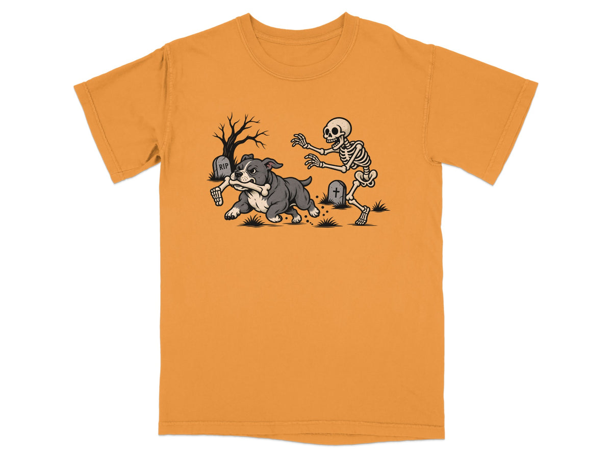 An orange t-shirt featuring a cartoon graphic of a skeleton chasing a dog holding a bone.