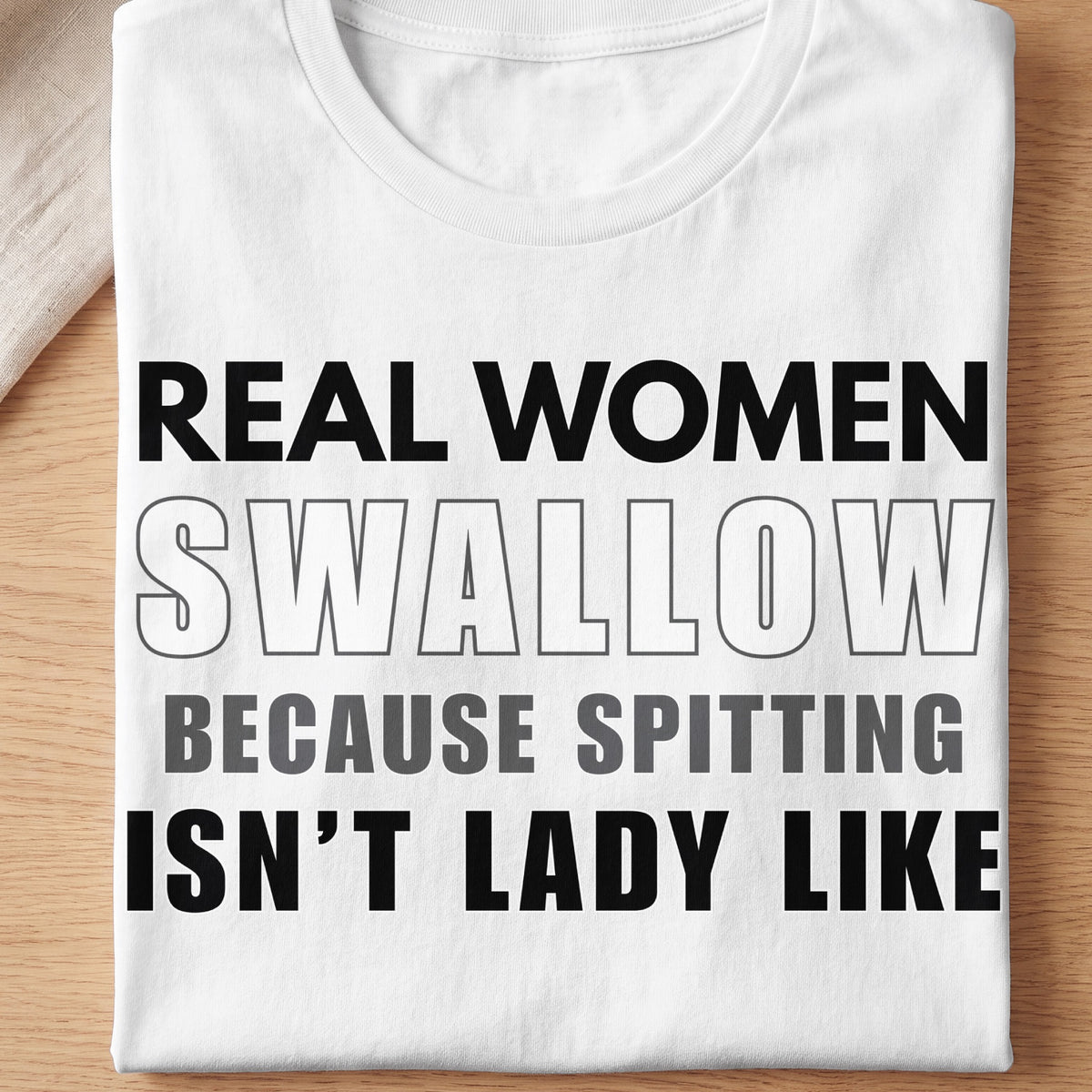 White t-shirt with black and gray text that reads "REAL WOMEN SWALLOW BECAUSE SPITTING ISN'T LADY LIKE".