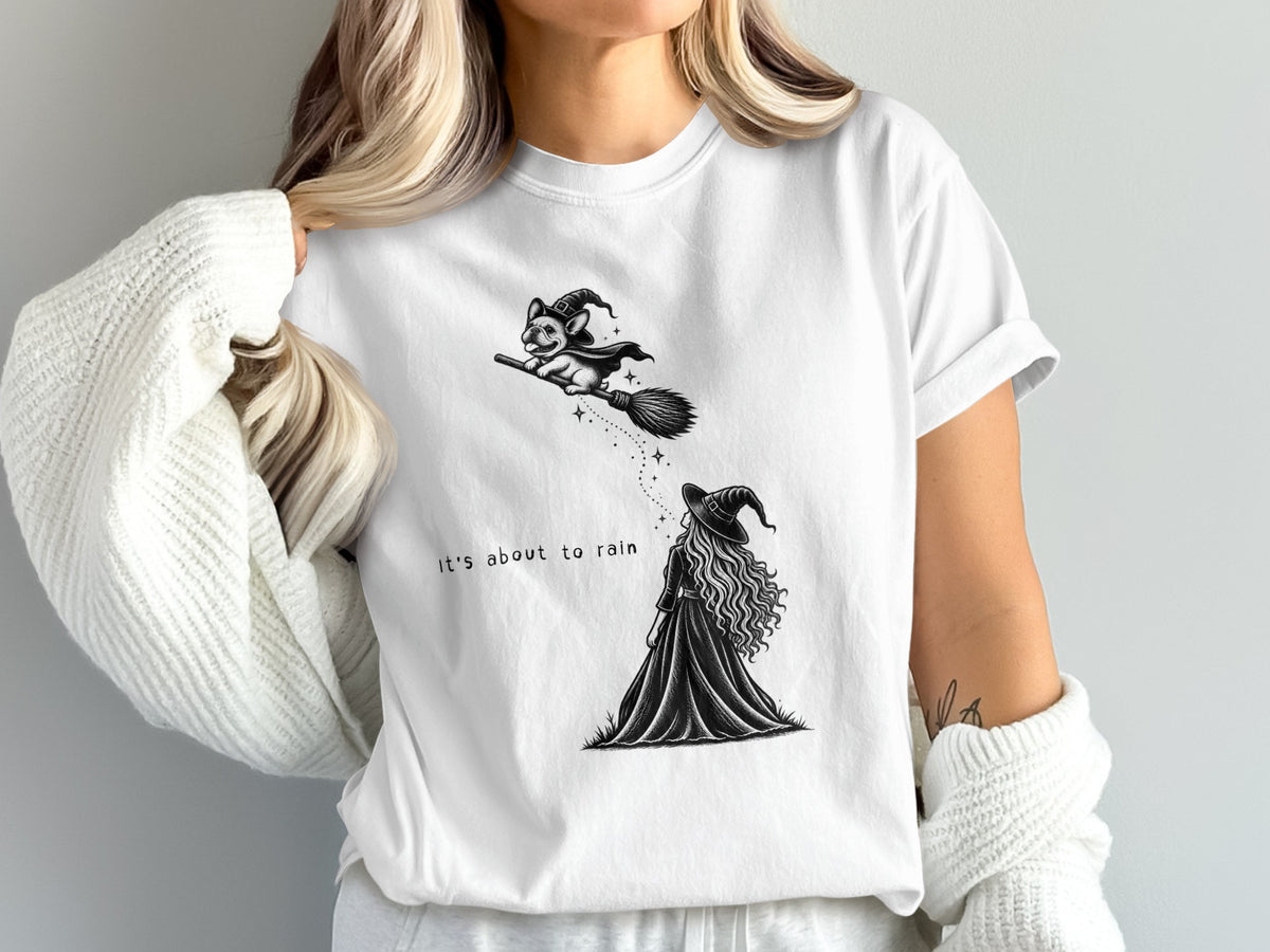 White t-shirt with witch and dog on broom, text "it's about to rain".