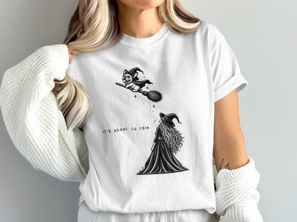 White t-shirt with witch and dog on broom, text "it's about to rain".