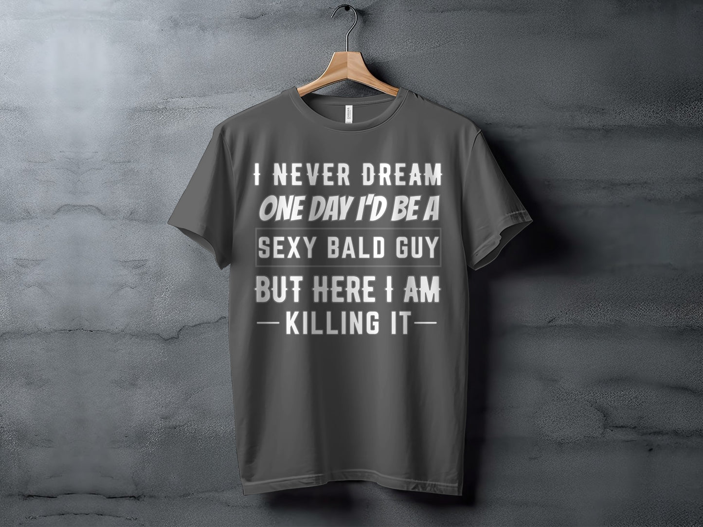 Dark gray t-shirt with text "I NEVER DREAM ONE DAY I'D BE A SEXY BALD GUY BUT HERE I AM - KILLING IT-".