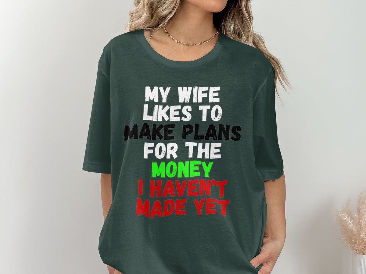 Dark green t-shirt with white, black, green, and red text reading "My wife likes to make plans for the money I haven't made yet."
