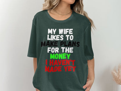 Dark green t-shirt with white, black, green, and red text reading "My wife likes to make plans for the money I haven't made yet."