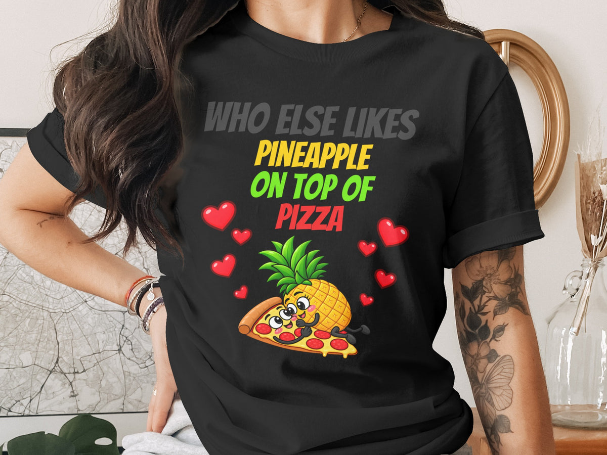 Black t-shirt with cartoon pineapple and pizza hugging, surrounded by hearts. Text reads "WHO ELSE LIKES PINEAPPLE ON TOP OF PIZZA".