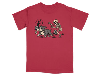 A red t-shirt featuring a graphic of a bulldog running away from an angry skeleton.