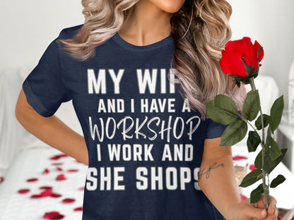 Dark blue t-shirt with white text: "MY WIFE AND I HAVE A WORKSHOP, I WORK AND SHE SHOPS."