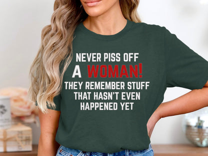 Dark green t-shirt with white text: "NEVER PISS OFF A WOMAN! THEY REMEMBER STUFF THAT HASN'T EVEN HAPPENED YET."