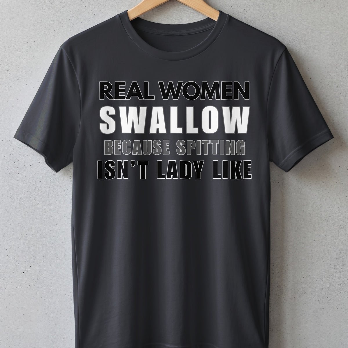 Dark t-shirt with white text "REAL WOMEN SWALLOW BECAUSE SPITTING ISN'T LADY LIKE".