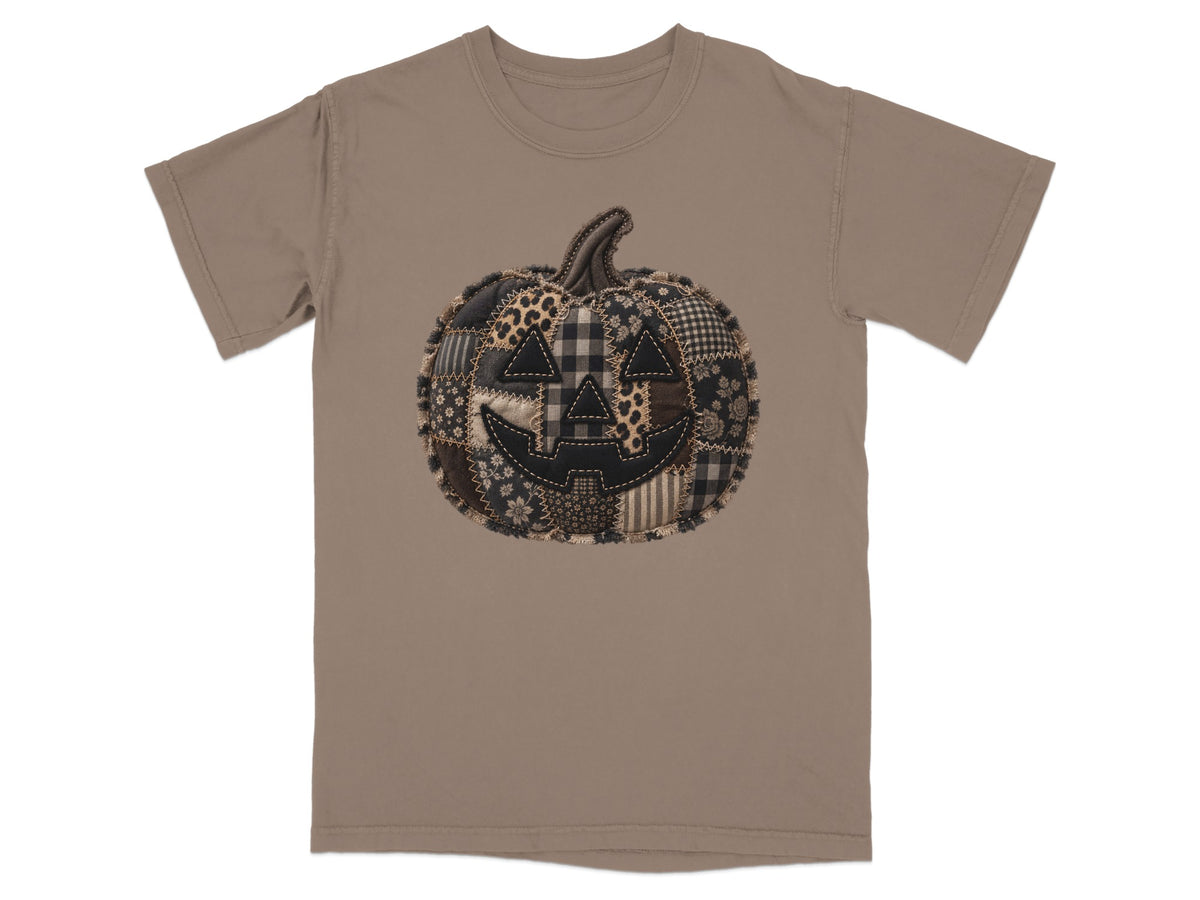 T-shirt with a patchwork Halloween pumpkin graphic on a taupe background.
