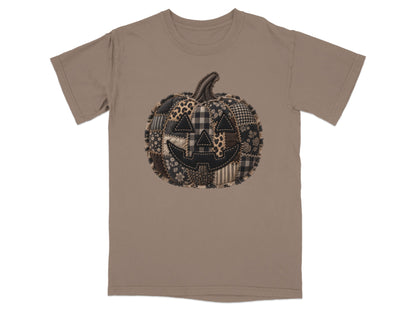 T-shirt with a patchwork Halloween pumpkin graphic on a taupe background.