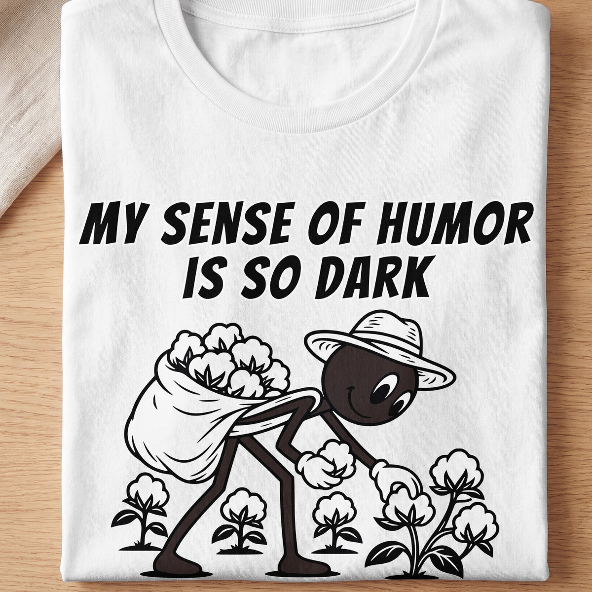 White t-shirt with black text "MY SENSE OF HUMOR IS SO DARK" and cartoon figure picking cotton.