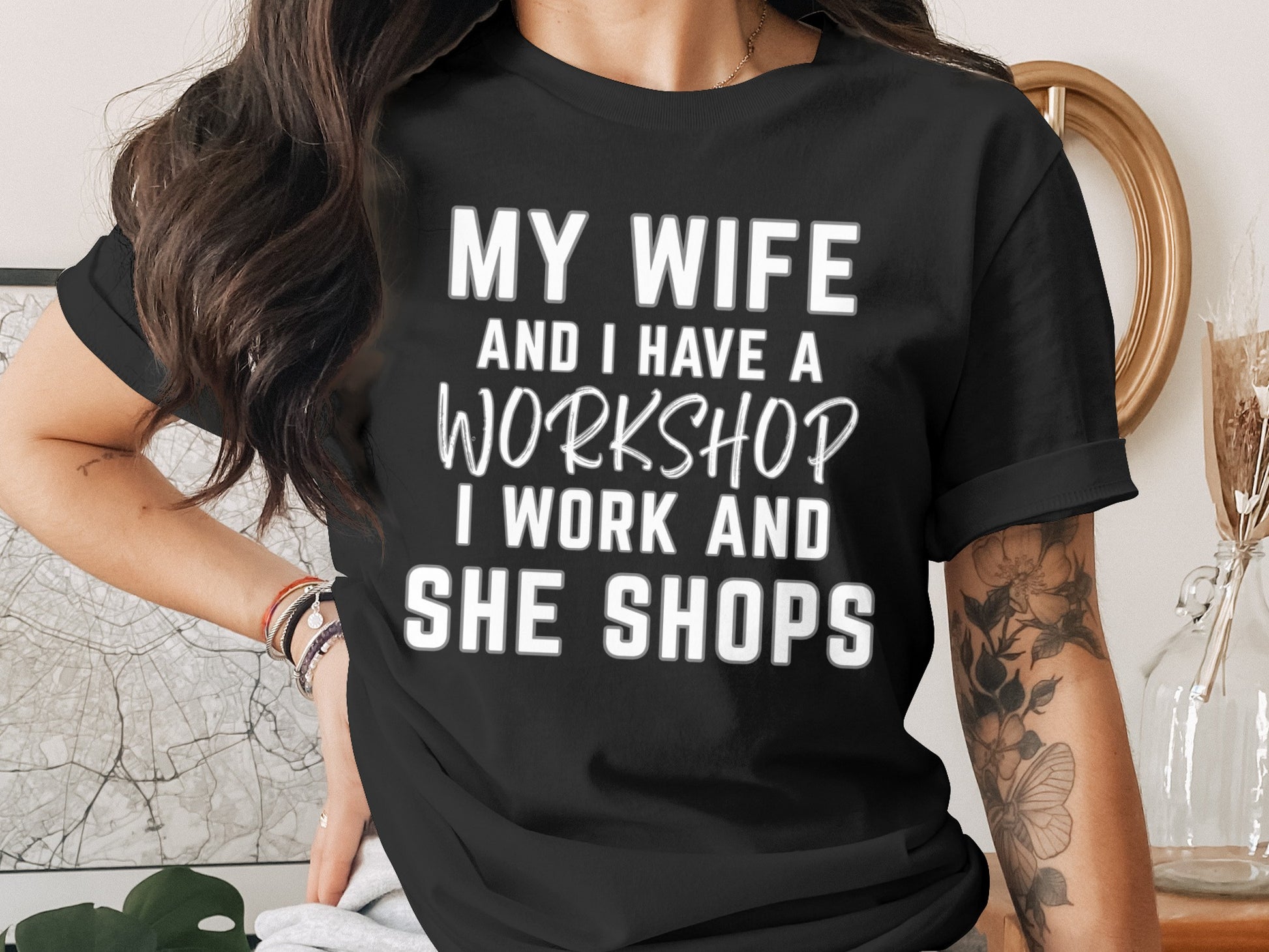 Black t-shirt with white text: "MY WIFE AND I HAVE A WORKSHOP. I WORK AND SHE SHOPS."