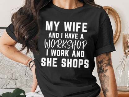 Black t-shirt with white text: "MY WIFE AND I HAVE A WORKSHOP. I WORK AND SHE SHOPS."