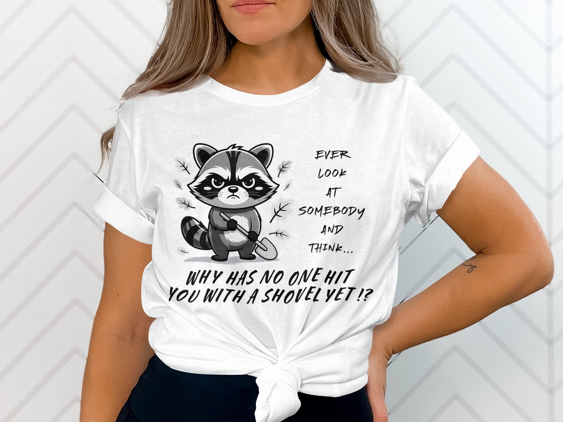 White t-shirt with a grumpy raccoon holding a shovel and text reading "Ever look at somebody and think... why has no one hit you with a shovel yet!?"