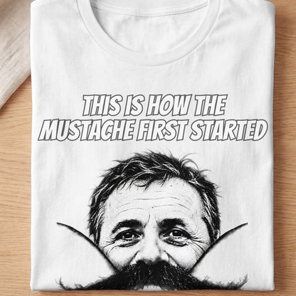 White t-shirt with graphic of a man's face and text "THIS IS HOW THE MUSTACHE FIRST STARTED".