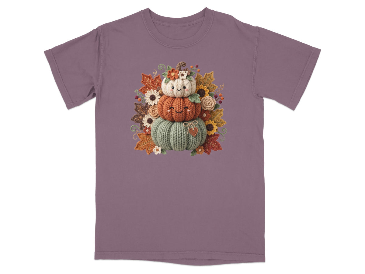 Stacked knitted pumpkins with smiling faces, surrounded by fall leaves and flowers.