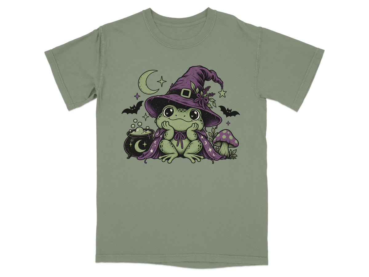 Sage green t-shirt featuring a cute green frog wearing a witch hat and cape, with bats and a cauldron.