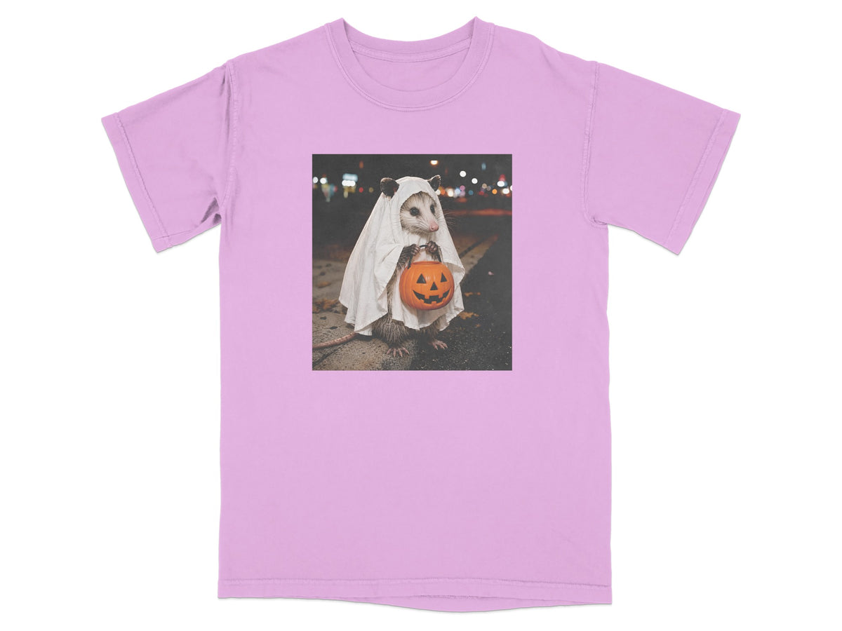 Opossum in ghost costume holding a jack-o'-lantern on a pink t-shirt.