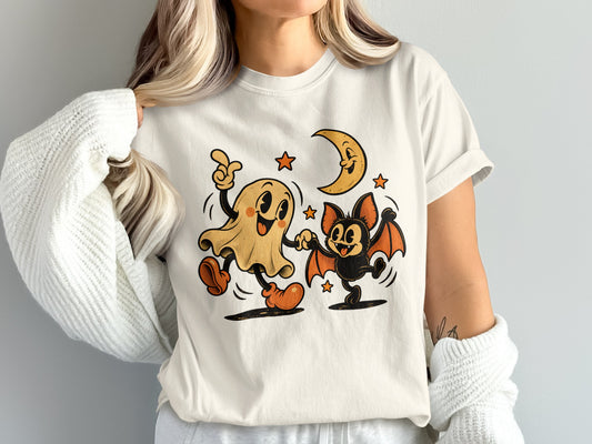 Ghost and bat dancing under a smiling moon and stars on a white shirt.