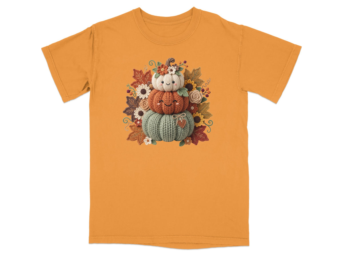Three knitted pumpkins stacked and decorated with autumn leaves and flowers.