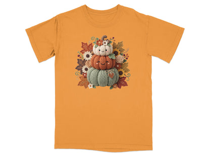 Three knitted pumpkins stacked and decorated with autumn leaves and flowers.