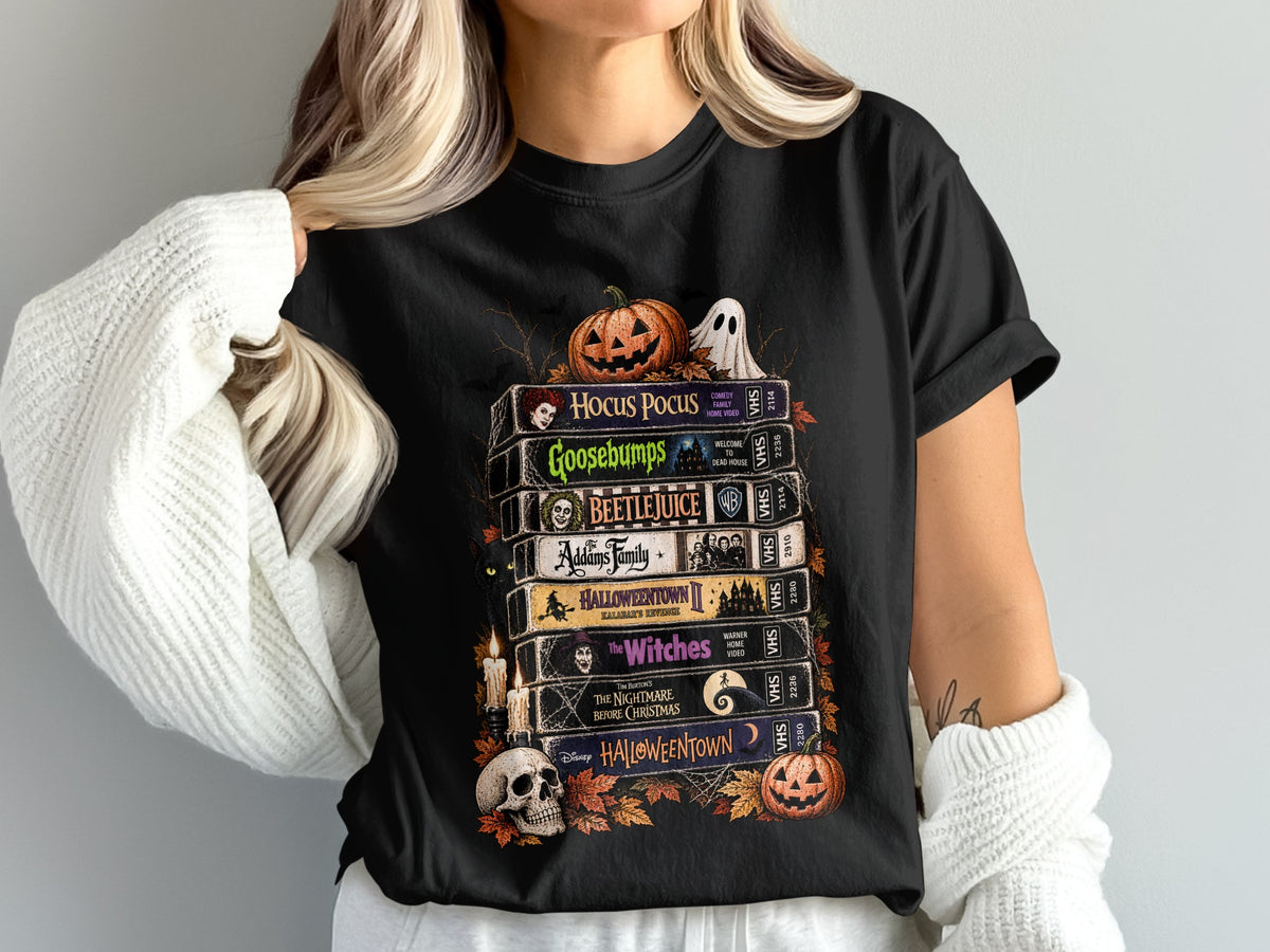 Black t-shirt featuring a stack of VHS tapes with Halloween movie titles and spooky graphics.