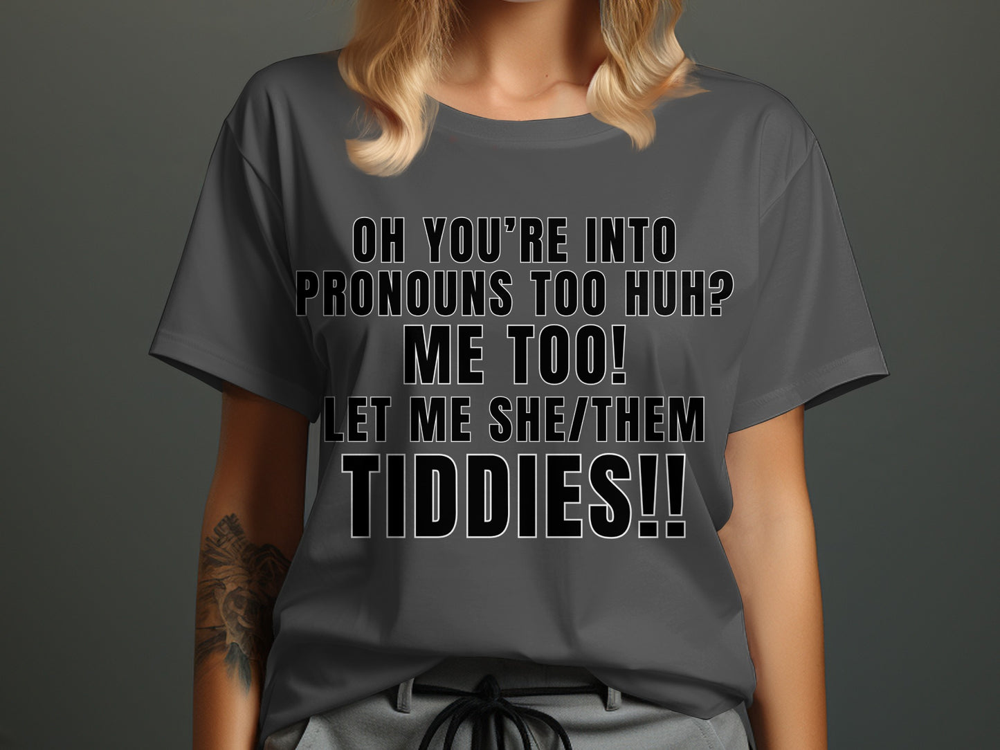 Dark gray t-shirt with black text: "OH YOU'RE INTO PRONOUNS TOO HUH? ME TOO! LET ME SHE/THEM TIDDIES!!"