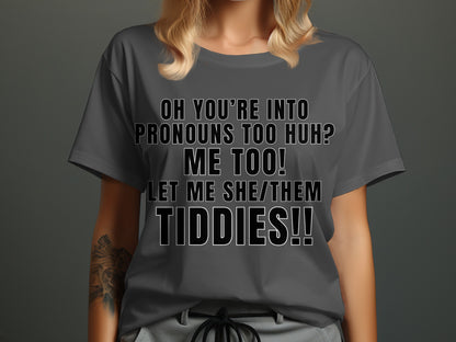 Dark gray t-shirt with black text: "OH YOU'RE INTO PRONOUNS TOO HUH? ME TOO! LET ME SHE/THEM TIDDIES!!"