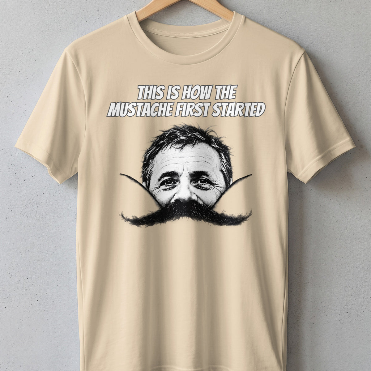 Cream t-shirt with "This is how the mustache first started" and a man's face with a large mustache.