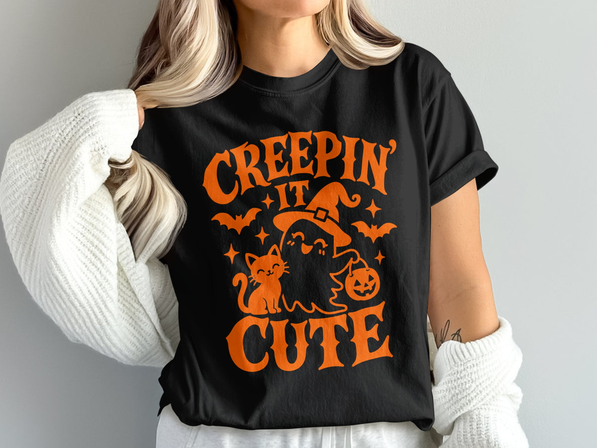 Black t-shirt with orange Halloween graphic: "Creepin' It Cute" with cat, ghost, and bats.