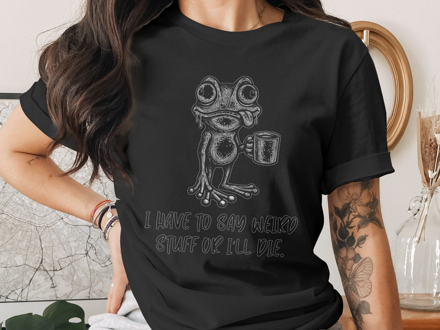 Black t-shirt with a drawing of a frog holding a mug and text that says "I HAVE TO SAY WEIRD STUFF OR I'LL DIE."