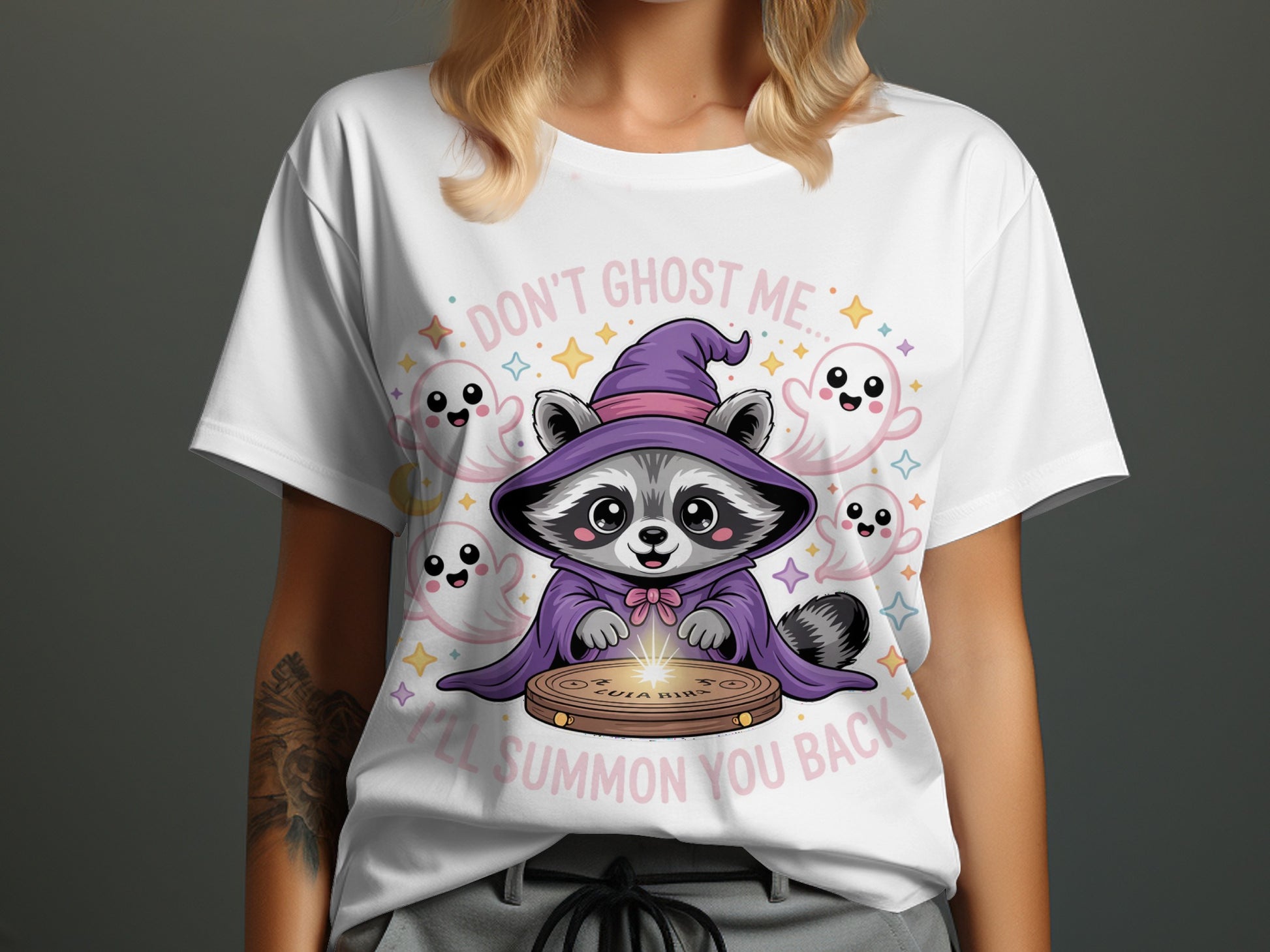 White t-shirt with cute raccoon in wizard outfit surrounded by ghosts and stars, text "DON'T GHOST ME... I'LL SUMMON YOU BACK".