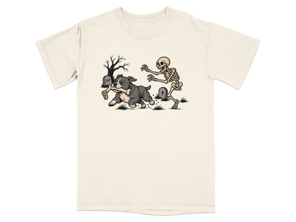 An off-white short-sleeve t-shirt features a graphic of a skeleton chasing a dog running with a bone in a graveyard.