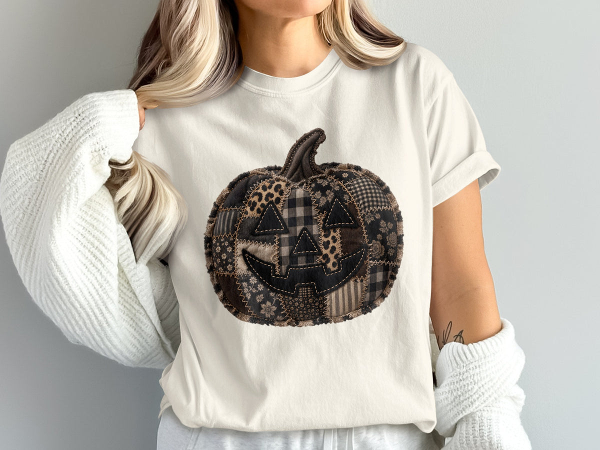 Patchwork Jack-o-lantern graphic on a cream t-shirt worn by a person.