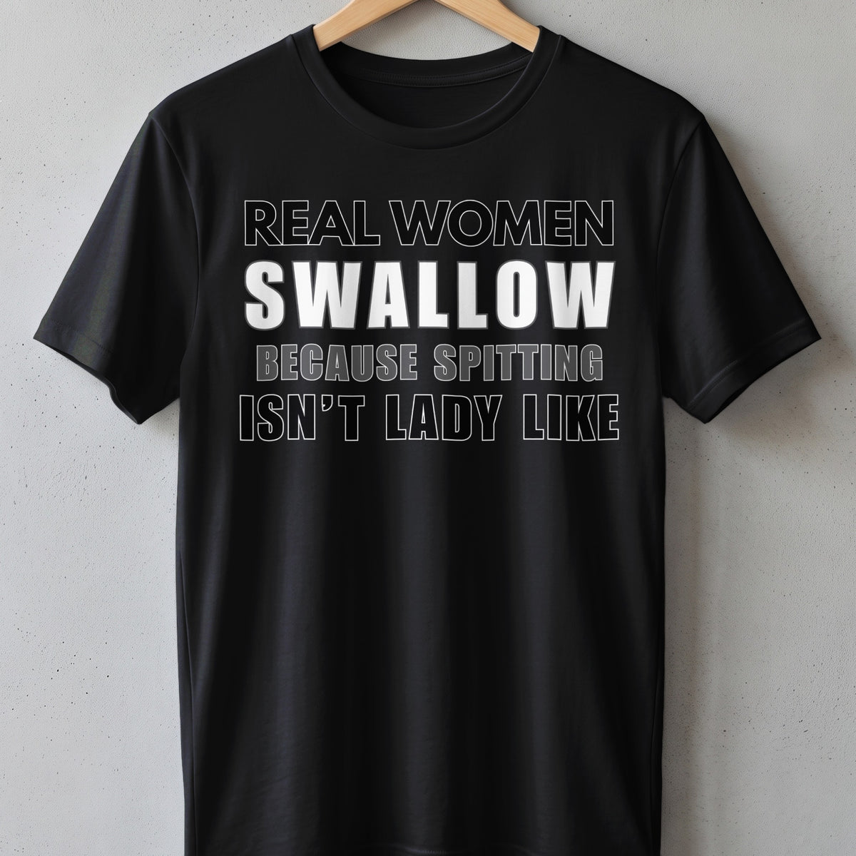 Black t-shirt with white text "REAL WOMEN SWALLOW BECAUSE SPITTING ISN'T LADY LIKE".