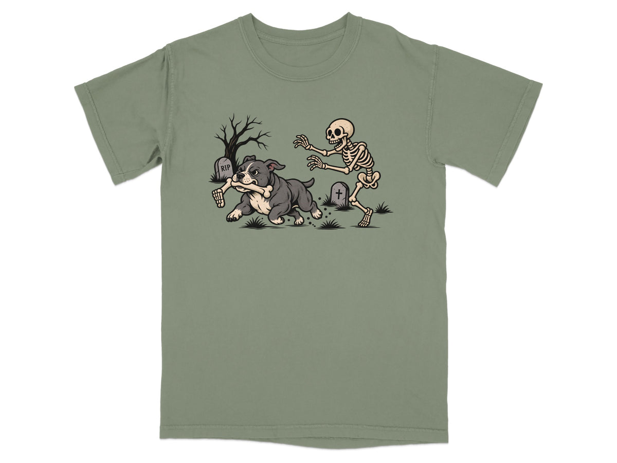 An olive green t-shirt featuring a cartoon design of a dog running away from a chasing skeleton in a graveyard.