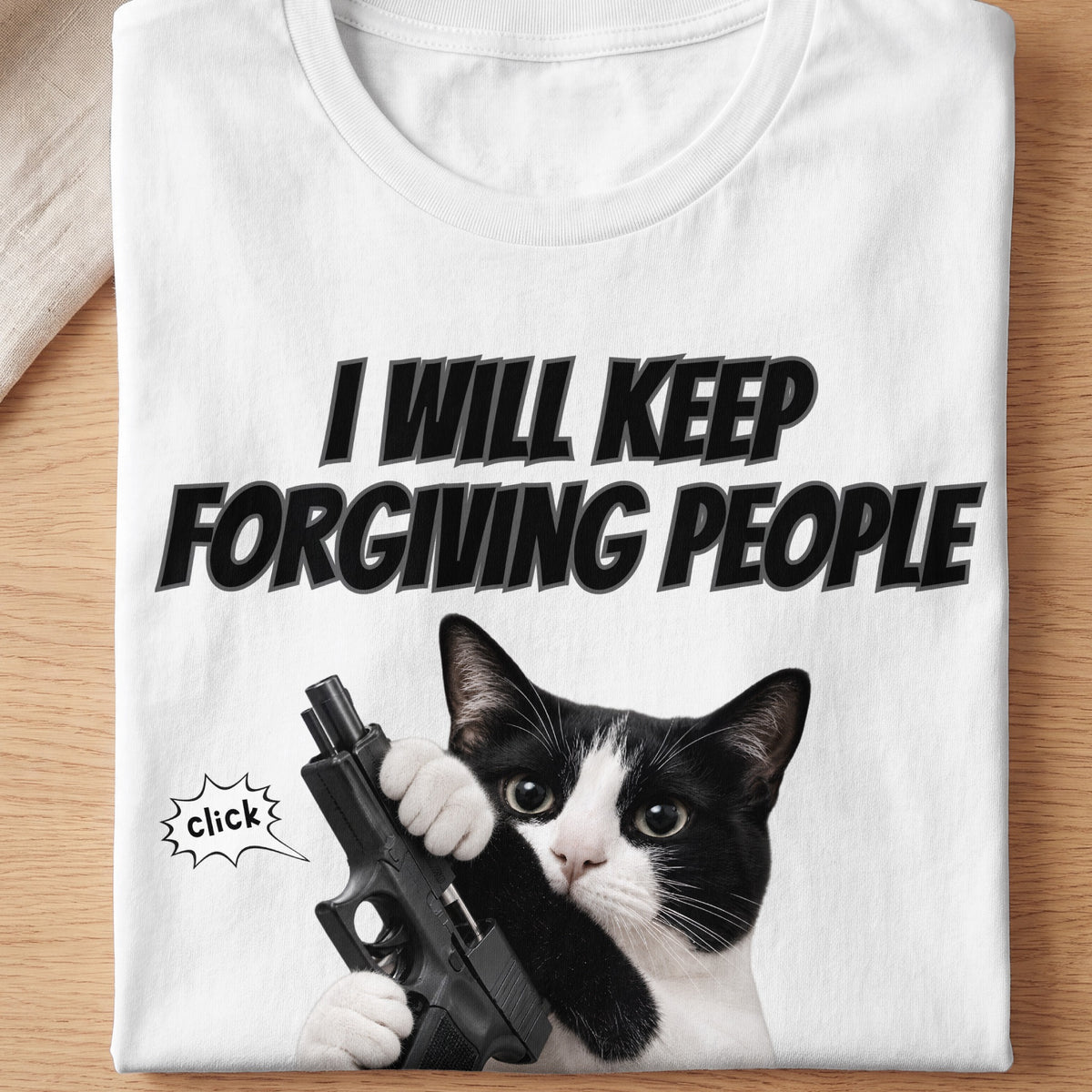 T-shirt with black text "I WILL KEEP FORGIVING PEOPLE" above a cat holding a gun.