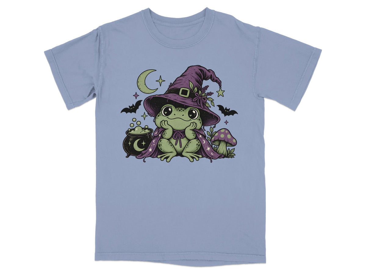 Periwinkle t-shirt featuring a green frog wearing a purple witch hat, cape, cauldron, and mushroom.