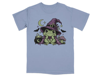 Periwinkle t-shirt featuring a green frog wearing a purple witch hat, cape, cauldron, and mushroom.