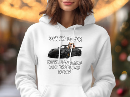 White hoodie with text "GET IN LOSER WE'RE IGNORING OUR PROBLEMS TODAY" and cartoon.