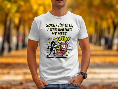 White t-shirt with cartoon graphic of person punching a steak. Text reads "SORRY I'M LATE, I WAS BEATING MY MEAT. POW!"