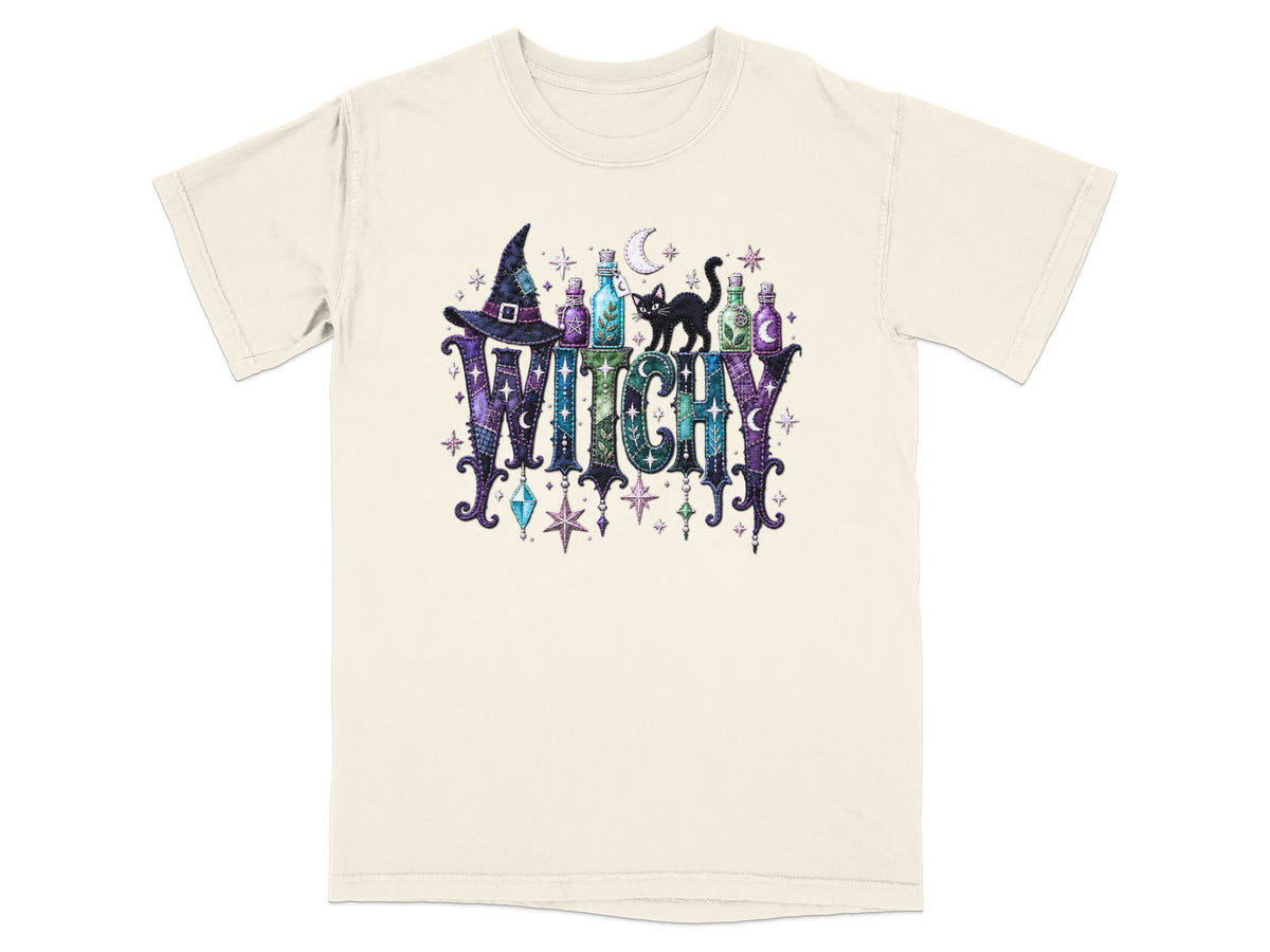 Cream t-shirt with "WITCHY" text, witch hat, potion bottles, black cat, and stars.