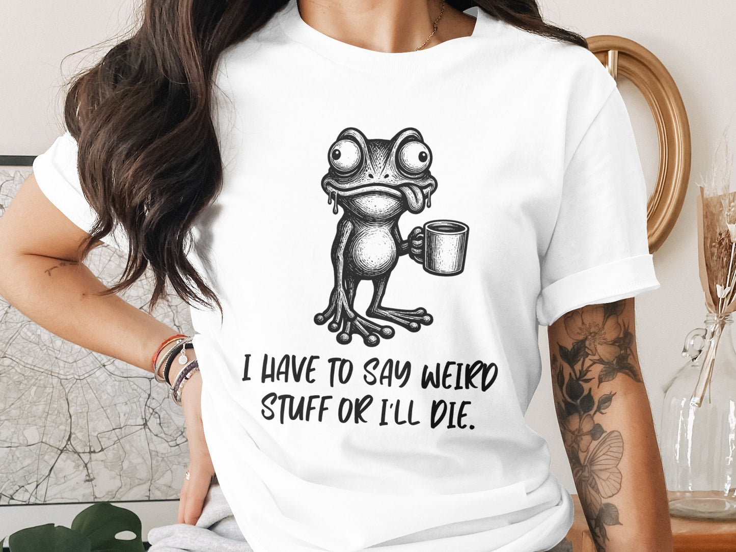 White t-shirt with a cartoon frog holding a coffee mug and text that says "I HAVE TO SAY WEIRD STUFF OR I'LL DIE."